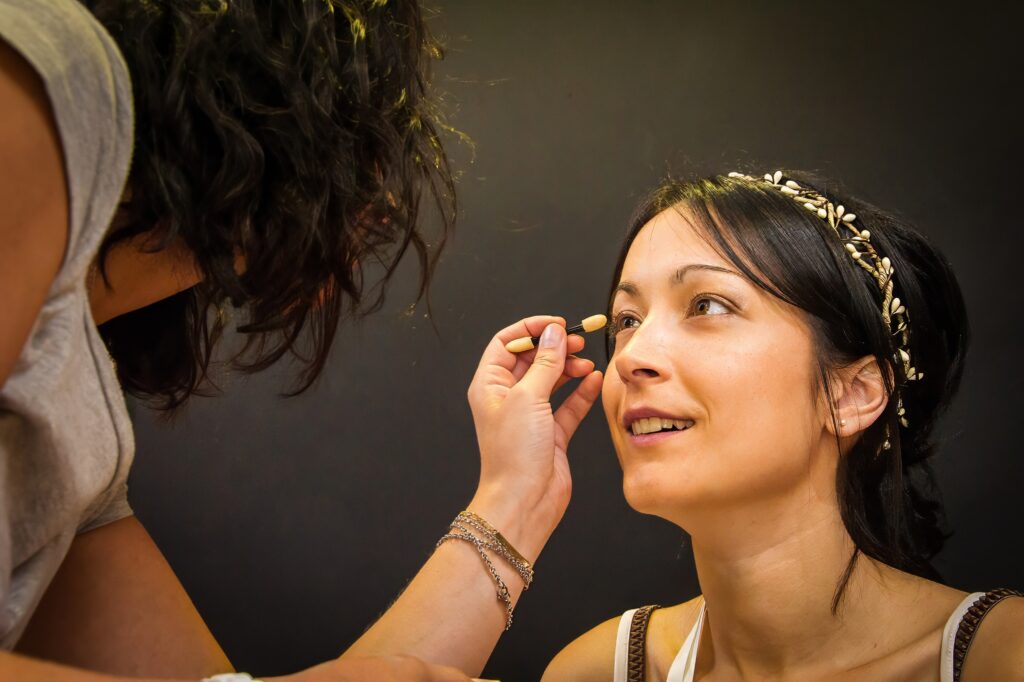 Mariée souriante regardant la maquilleuse pendant la séance de maquillage