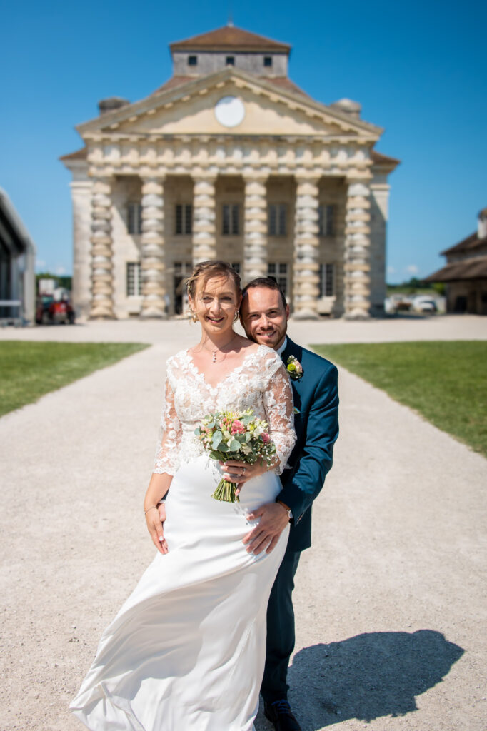 Mariés posant avec un bouquet devant les Salines d'Arc-et-Senans