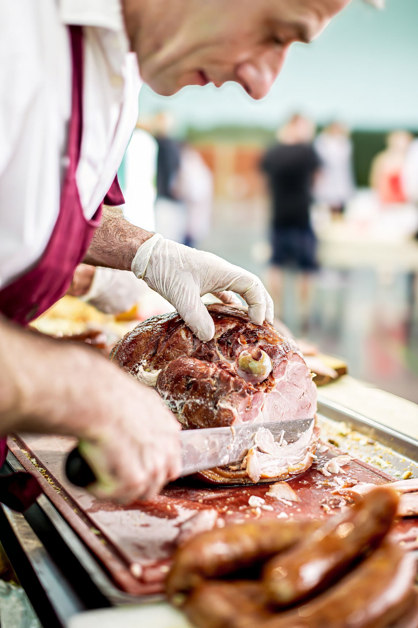 Chef en tablier rouge et gants blancs découpant une pièce de viande sur une planche à découper au vin d'honneur