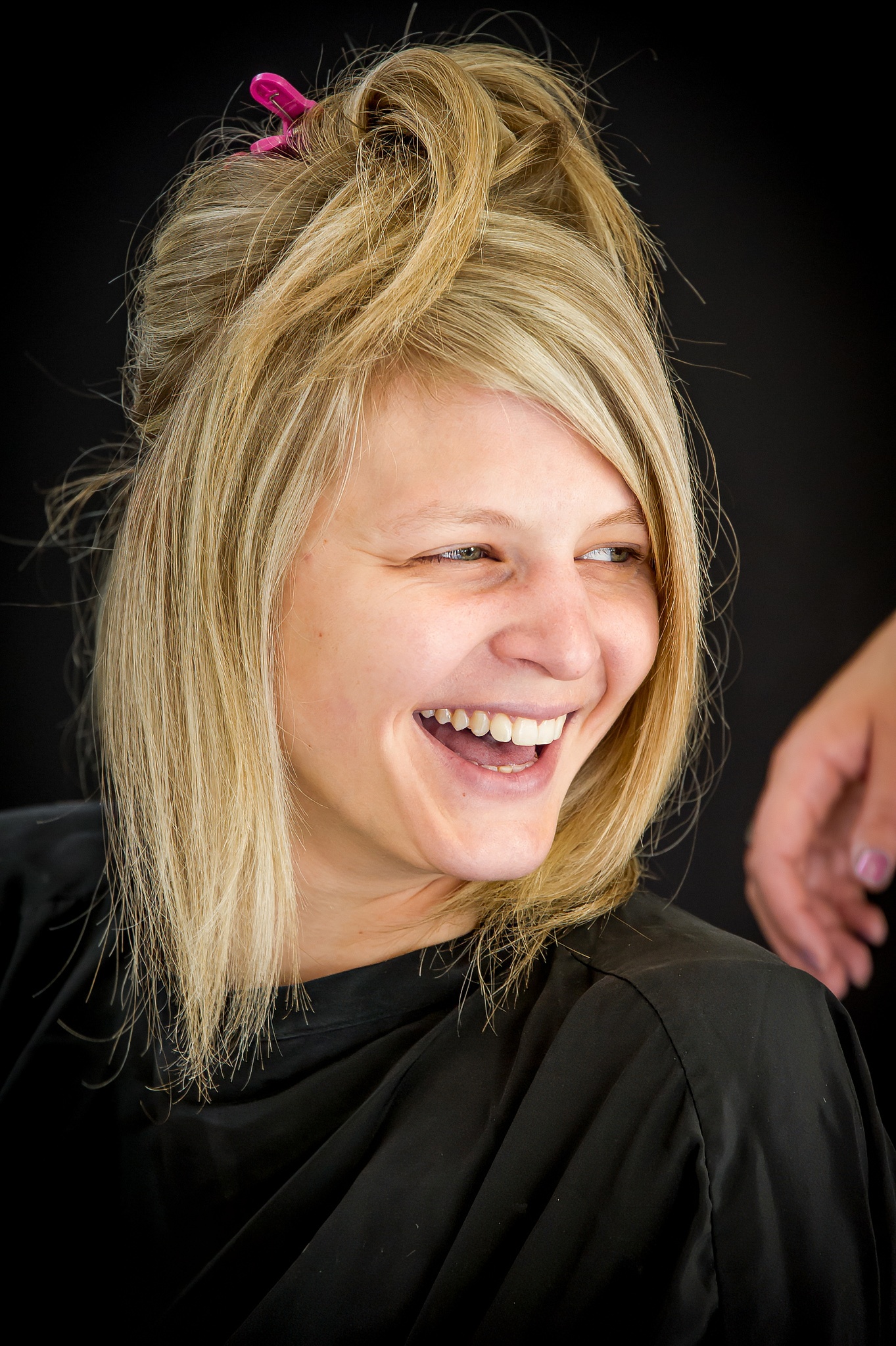 La mariée souriante avec des cheveux attachés, en préparation, vêtue d'une cape de coiffure