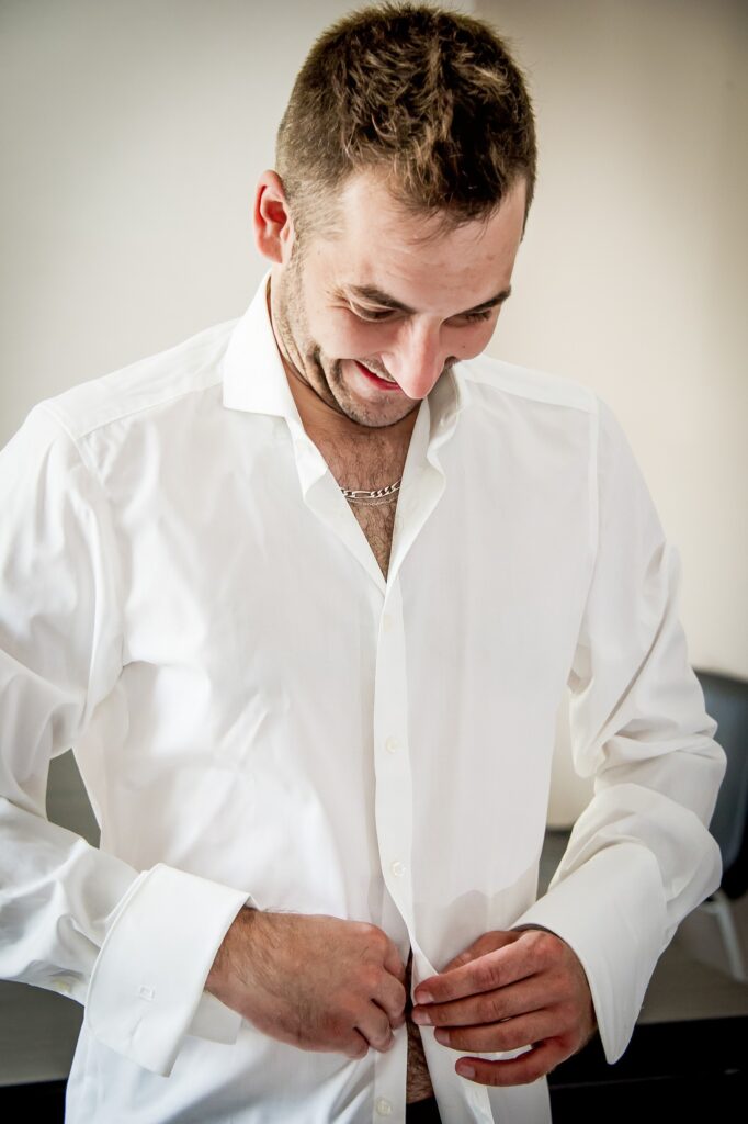 Marié souriant boutonner une chemise blanche