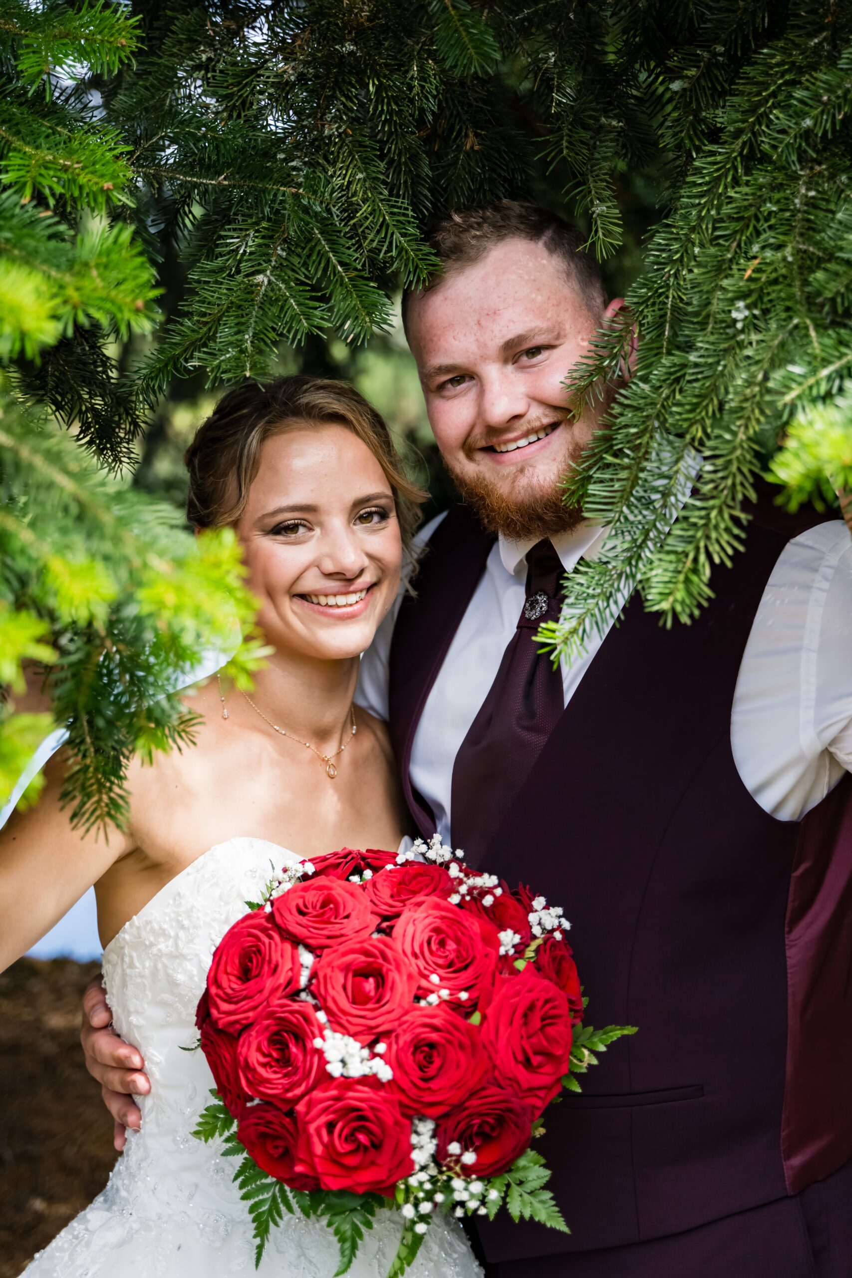 Mariés souriant sous les arbres avec bouquet de roses rouges