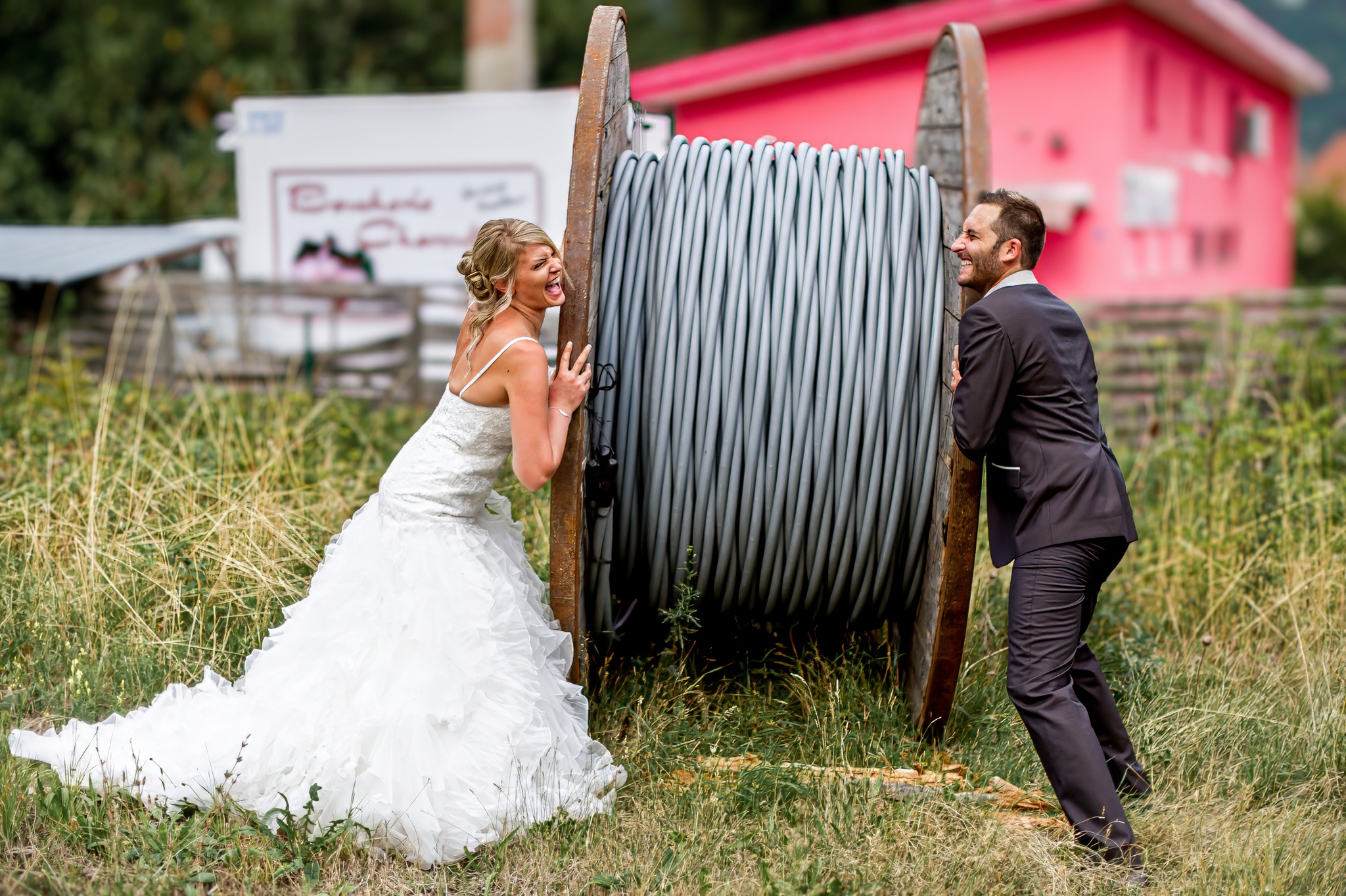 Couple de mariés s'amusant avec un énorme tambour de câble en plein air pendant une séance Trash the dress