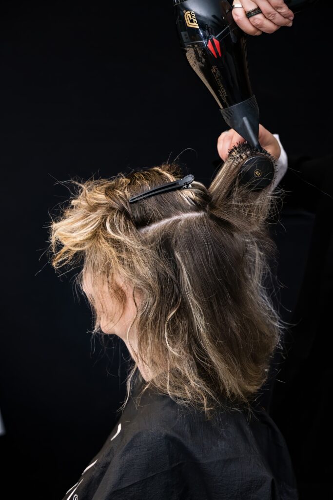 Coiffeuse séchant les cheveux avec un sèche-cheveux et une brosse ronde